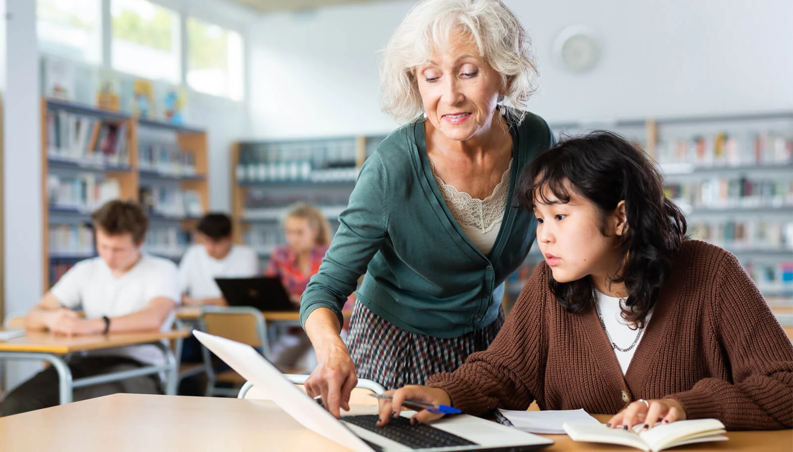 Eine Schulbegleiterin schaut einer Schülerin über die Schulter.