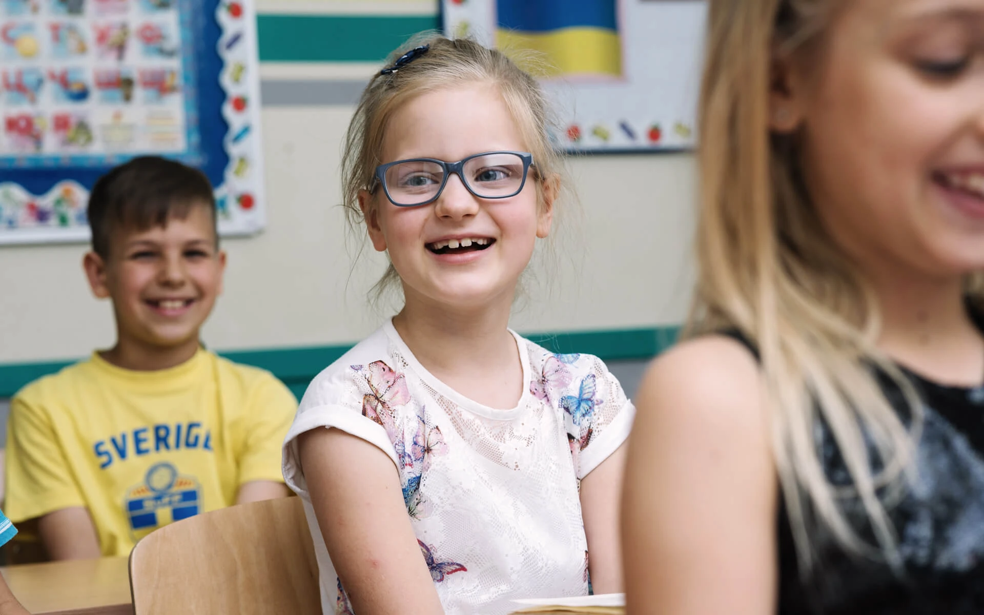 Drei Kinder sitzen im Klassenraum und lachen.