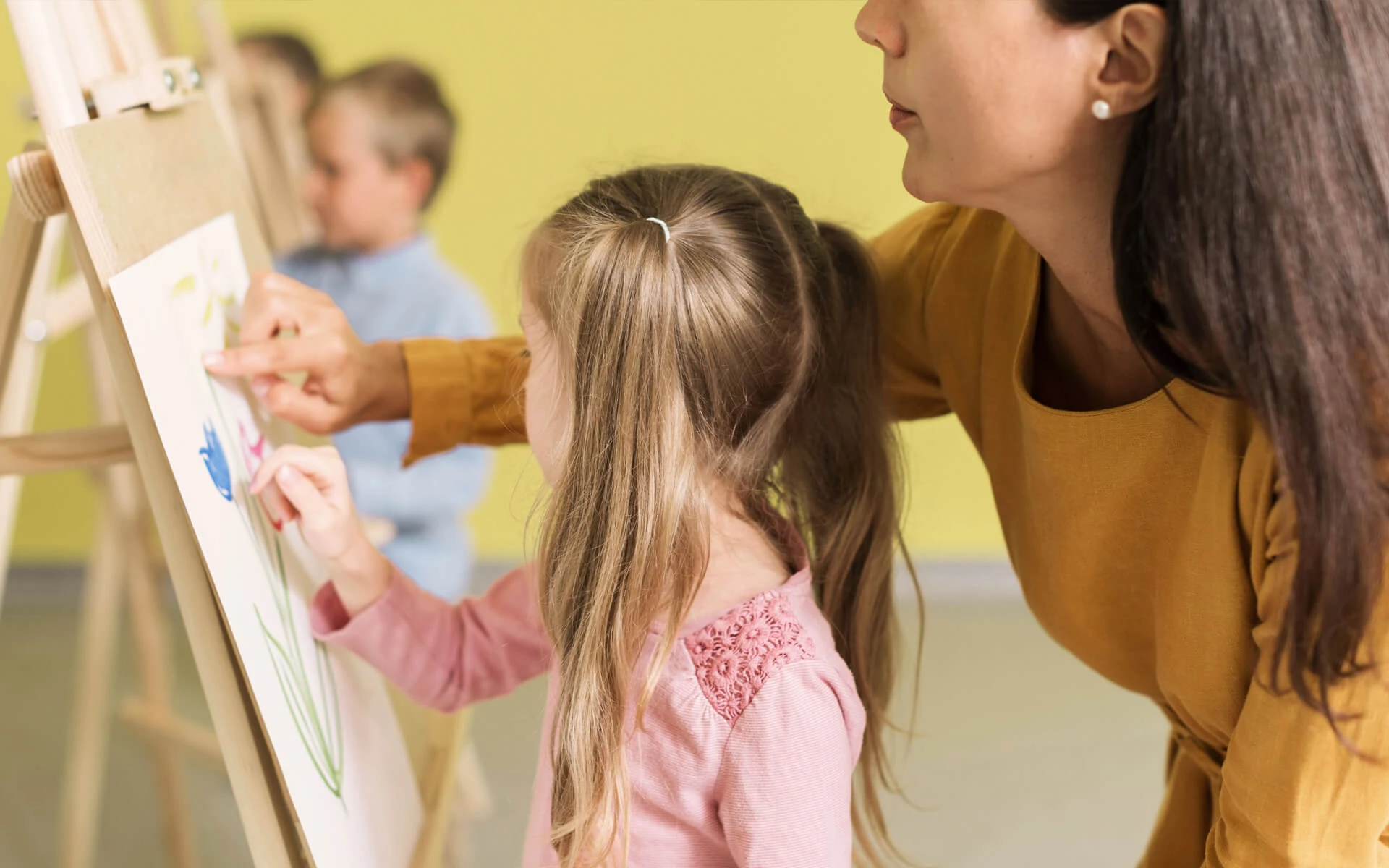 Eine Schulbegleiterin hilft einem Kind beim Malen auf einer Leinwand.