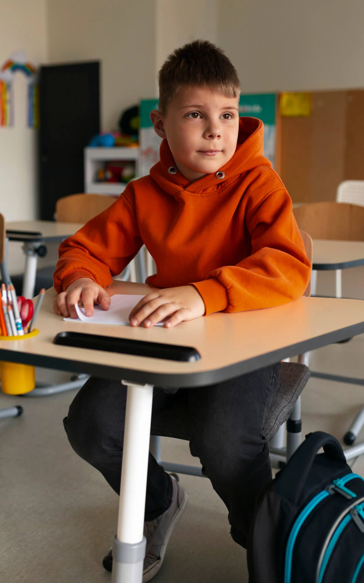 Ein Junge in einem orangefarbenen Pullover sitzt in einem Klassenraum.